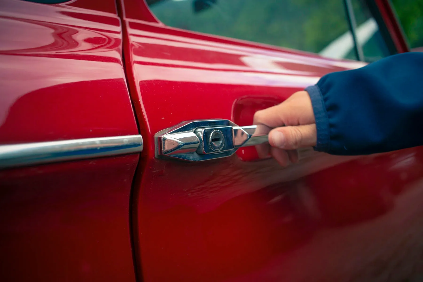 Close-up of a hand at the door lock cylinder of a red car during a vehicle lockout