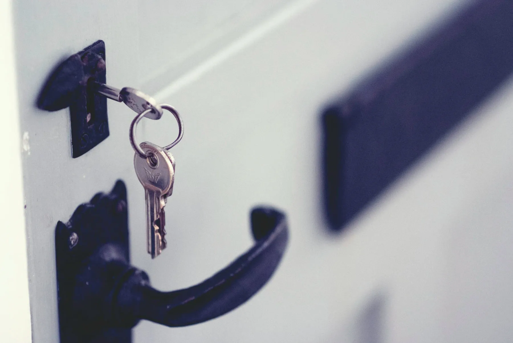House keys left hanging in the cylinder of a white front door